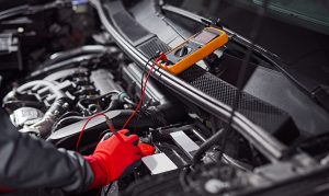 Crop,Anonymous,Technician,In,Protective,Gloves,Measuring,Voltage,Of,Automobile